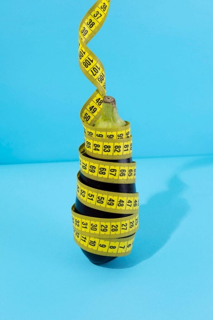 Metaphor-like photograph with a measuring tape around an eggplant depicting the act of measuring a penis to use a chastity cage.